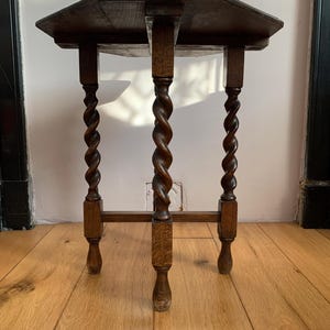 Könnte beinhalten: Kleiner, antiker Holztisch mit dunkelbraunem Finish. Die achteckige Tischplatte ruht auf drei Beinen mit gedrehtem Seildesign, jeweils etwa 61 cm hoch. Der Tisch steht auf einem Holzboden.