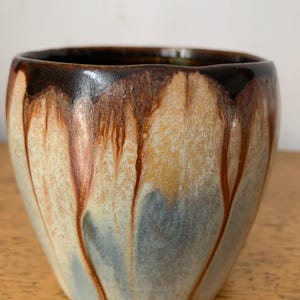 Peut inclure: Un vase en céramique avec un glaçage blanc et des gouttes brunes et orange. Le vase a une forme arrondie et une lèvre légèrement évasée.