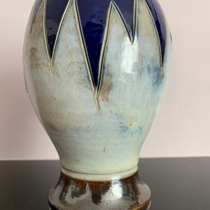 Peut inclure: Un vase en céramique avec un glaçage blanc et un motif géométrique bleu. Le vase a une base large et un col étroit.