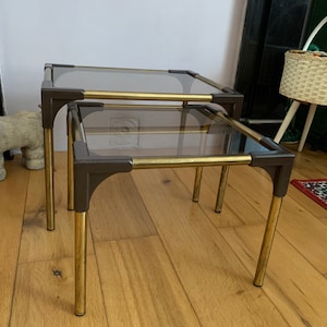 May include: A set of two nesting glass and brass end tables. The tables have a smoked glass top and brass legs and trim.