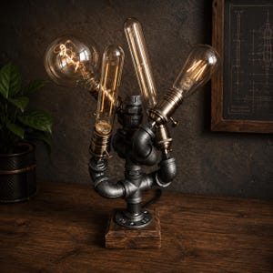 Può includere: Lampada da tavolo in stile industriale con lampadine Edison a vista e struttura in tubi metallici. La lampada ha una base in legno e una finitura scura, creando un'estetica vintage. Le lampadine sono di colore ambra caldo, che fornisce una luce soffusa. La lampada è alta circa 30 cm.