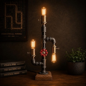 May include: Industrial-style lamp made from black pipes, featuring three Edison-style light bulbs. The lamp has a red valve and sits on a wooden base. A framed print reading "INDUSTRIAL PIPING" is visible in the background.