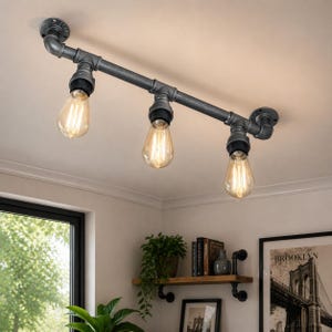 Könnte beinhalten: Industrielle Deckenleuchte mit drei freiliegenden Edison-Glühbirnen. Die Leuchte besteht aus grauen Metallrohren und -armaturen, die an der Decke befestigt sind. Die tropfenförmigen Glühbirnen haben sichtbare Glühfäden und erzeugen ein warmes Licht.