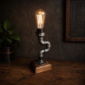 Può includere: Lampada da tavolo in stile industriale con una lampadina Edison vintage. La lampada presenta un design a tubo metallico e una base in legno. La lampadina emette una calda luce. La lampada è alta circa 30 cm.