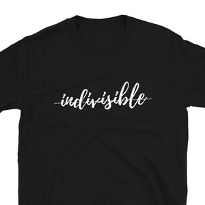 May include: Black short-sleeved t-shirt with the word "indivisible" written in white cursive lettering.