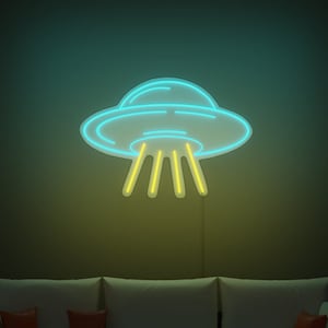 May include: A blue neon UFO sign with yellow neon beams of light. The sign is mounted on a wall above a white sofa with orange throw cushions.