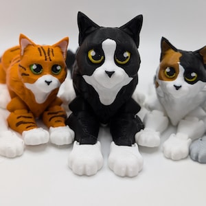 May include: Five 3D printed cat figurines, each with a different color and pattern. The cats are all in a sitting position with their heads tilted slightly to the side. The cats are all looking at the camera.