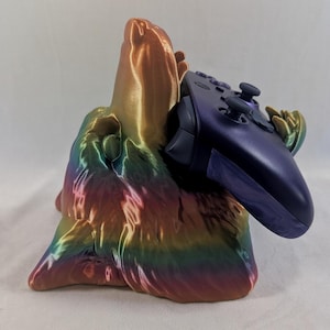 May include: A 3D printed rainbow colored wolf head game controller stand with a purple Xbox controller resting in it.