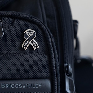 May include: A black travel bag with a silver ribbon pin that says "PSA 5/12" and "PAT23". The bag has a Briggs & Riley logo on the front.