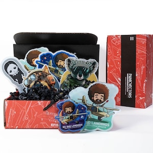 May include: A box filled with colorful stickers featuring cartoon characters and airplanes. The stickers have text that reads "Trust Me", "No Bad Landings", "Gid Landings", and "Panic Vectors".