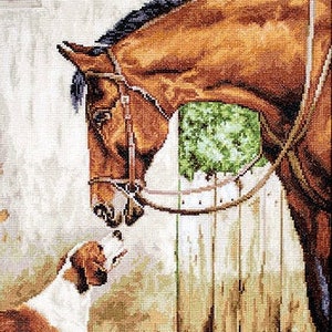 May include: A brown horse with a black mane and tail looks down at a white and brown dog. The horse is wearing a brown leather bridle and is tied to a wooden fence. The dog is looking up at the horse.