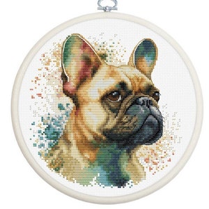May include: A cross-stitch embroidery of a French Bulldog in a round, white hoop. The dog's fur is a mix of tan, brown, and black, with colorful watercolor-like accents. The background is white, and the hoop has a metal clasp.