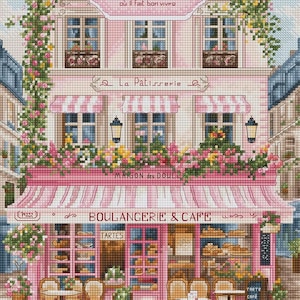 May include: A cross-stitch pattern depicting a pink Parisian building with a storefront labelled BOULANGERIE & CAFE. The scene features climbing roses, striped awnings, outdoor tables with chairs, and a sign reading PARIS CAFÉ VIVÉ où il fait bon vivre.