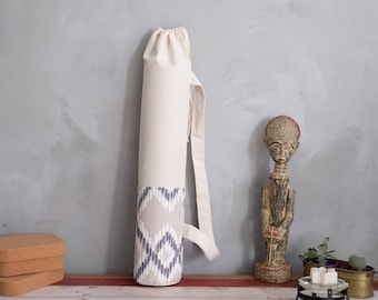 May include: A white canvas yoga mat bag with a grey and beige geometric pattern at the bottom. The bag has a long strap for carrying over the shoulder.