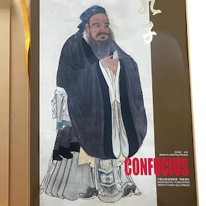 May include: A book cover featuring a portrait of Confucius in traditional robes, with the Chinese characters for Confucius in gold, the text CONFUCIUS in red, and publisher information including Shangdong Publishing Group China Qilu Press.