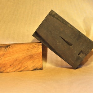 May include: A vintage wooden printing block with the letter "A" carved into it. The block is made of dark wood and has a worn, aged appearance. The letter "A" is raised and has a sharp, defined edge.