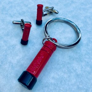 May include: A set of three red and black miniature post box cufflinks and a keyring. The cufflinks and keyring are all in the shape of a post box.