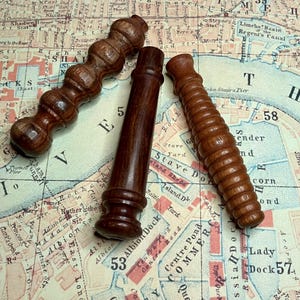 May include: Four antique wooden objects in shades of brown, including fluted, cylindrical, and bulbous designs. They are displayed on a vintage map, showcasing their intricate craftsmanship.