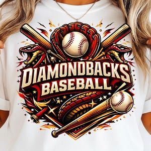 May include: White t-shirt featuring a baseball-themed graphic. The design includes a baseball, glove, bats, and the text "Diamondbacks Baseball" in a bold, stylized font. The graphic is in shades of red, gold, and black.