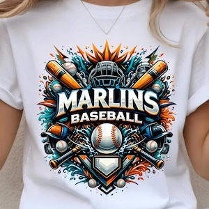 May include: White t-shirt featuring a colorful baseball-themed graphic. The design includes the text "Marlins Baseball" with baseball bats, helmets, and a baseball. The graphic is in shades of orange, blue, and teal.