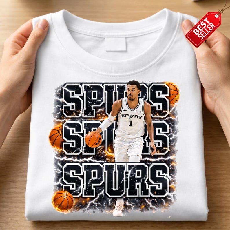 Pu&ograve; includere: Felpa bianca girocollo con grafica di un giocatore di basket in uniforme Spurs, con la scritta "SPURS" in grassetto e bordata. Sono inclusi anche palloni da basket ed effetti di fulmini.