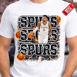Pu&ograve; includere: T-shirt bianca con un giocatore di basket in uniforme Spurs, con la parola "SPURS" in grassetto e contornata. Il design include palloni da basket e un'etichetta "Best Seller".