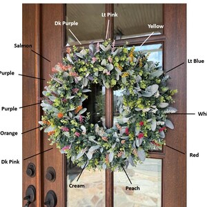 May include: A circular wreath featuring green foliage and various colored floral accents labeled as Dk Purple, Lt Pink, Yellow, Salmon, Lt Purple, Med Purple, Orange, Dk Pink, Cream, Peach, Lt Blue, White, and Red, displayed on a brown wooden door.