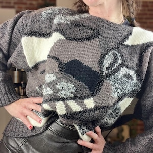 May include: A gray, white, and black patterned sweater with a loose fit and a slightly off-the-shoulder neckline.