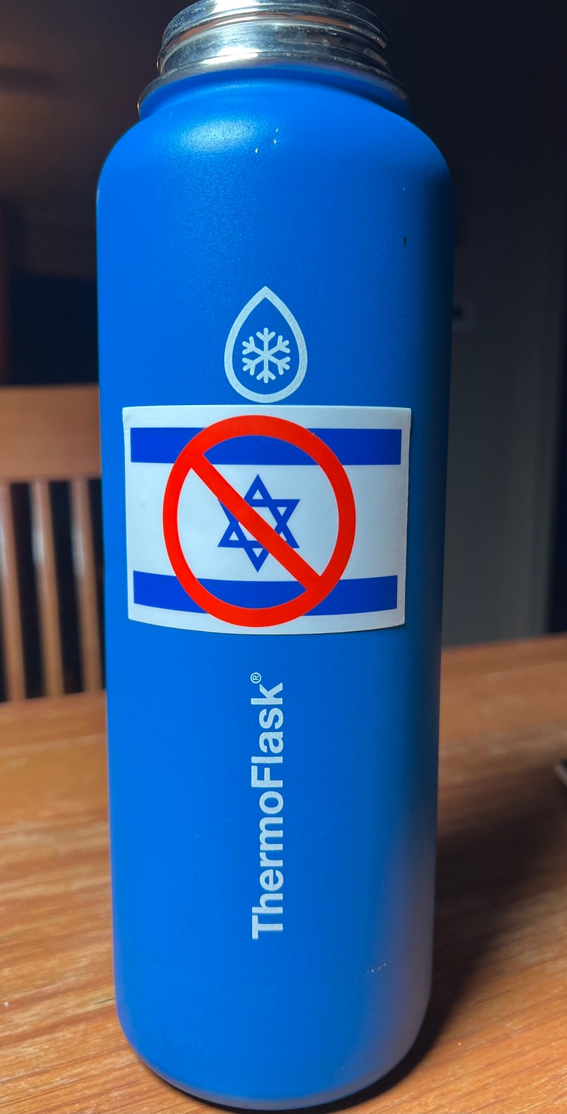 May include: Blue ThermoFlask water bottle with a silver lid. A sticker on the bottle features the Israeli flag with a red prohibition symbol over it. The bottle has a white logo and the words "ThermoFlask" printed on it.