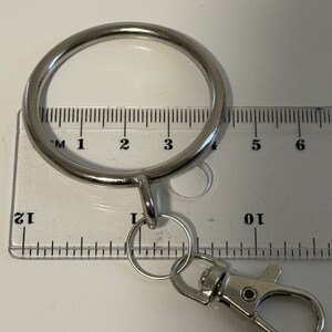 Puede incluir: Anillo de llaves plateado con un anillo redondo grande y un anillo m&aacute;s peque&ntilde;o con un clip. El anillo se mide con una regla, mostrando que tiene aproximadamente 10 cm de di&aacute;metro.