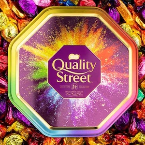 May include: A close-up of a Quality Street tin with a colourful design. The tin is surrounded by a variety of colourful wrapped chocolates.