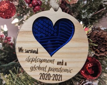 Peut inclure: Une décoration de Noël en bois avec un cœur bleu et le texte "We survived deployment and a global pandemic 2020-2021".