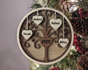 Peut inclure: Une décoration de Noël en bois en forme d'arbre avec quatre cœurs suspendus aux branches. Les cœurs sont inscrits avec les noms "Andrea", "Rafael", "Sarah" et "Mikey". L'année "2020" est inscrite sur le tronc de l'arbre.