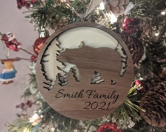 Peut inclure: Une décoration de Noël ronde en bois avec une silhouette d'ours brun, des sapins et le texte "Smith Family 2021".