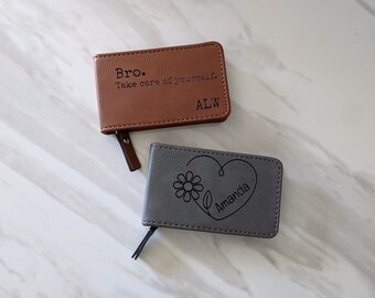 Peut inclure: Deux petites pochettes en cuir avec des fermetures à glissière. Une pochette est marron avec le texte "Bro. Take care of yourself. ALW" et l'autre pochette est grise avec un motif de cœur et de fleur et le texte "Amanda".