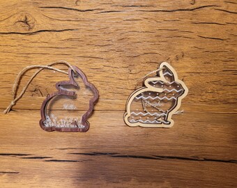 Peut inclure: Deux décorations de lapin en bois avec un motif blanc et gris. Le lapin à gauche porte le nom Millie gravé. Le lapin à droite porte le nom Vaughn gravé.