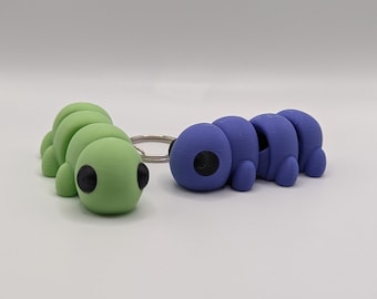 Peut inclure: Deux porte-clés en forme de chenille colorés, l'un vert et l'autre violet, avec des yeux noirs. Les porte-clés sont en plastique et ont un anneau métallique pour les attacher aux clés.