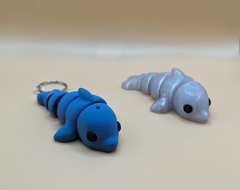 Peut inclure: Deux petits porte-clés en forme de dauphin, l'un bleu et l'autre argenté. Le dauphin bleu a un anneau argenté pour l'attacher aux clés. Les deux dauphins ont des yeux noirs.
