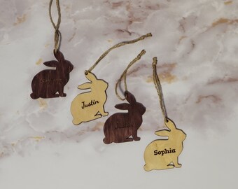 Peut inclure: Quatre ornements en forme de lapin en bois avec des cordes en jute. Deux sont en bois clair, deux sont brun foncé. Chaque lapin porte un nom gravé : Sophia, Justin, et deux avec le nom Justin et un avec le nom Sophie.
