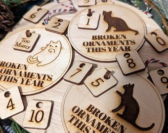 Peut inclure: Un ensemble d'ornements en bois sur le thème du chat. Les ornements sont ronds et portent le texte "Broken Ornaments This Year". Il y a aussi de plus petits ornements carrés avec des numéros dessus. Les ornements sont décorés d'une silhouette de chat et du texte "Too Many".