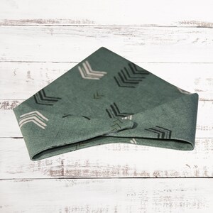 May include: A green bandana with a white and black arrow pattern. The bandana is folded into a triangle shape.
