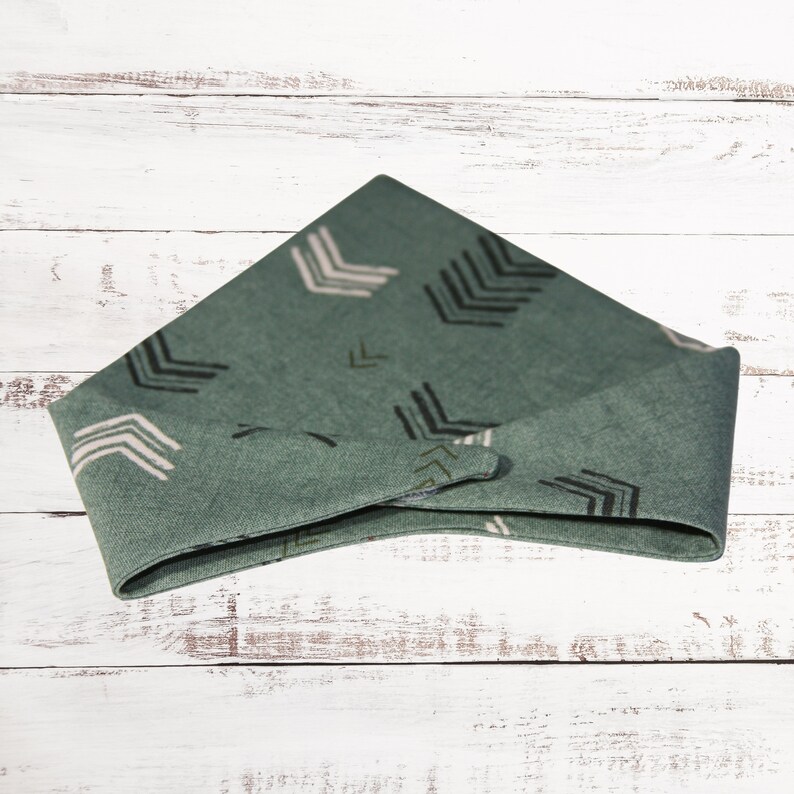May include: A green bandana with a white and black arrow pattern. The bandana is folded into a triangle shape.