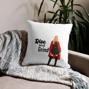 May include: White throw pillow with a red and black illustration of a woman wearing a red coat and black boots. The text "Rise and Grind" is printed in black on the pillow.