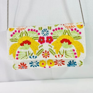 Pu&ograve; includere: Clutch bianca in perline con un design floreale con perline gialle, rosse, arancioni, rosa, verdi e blu. La borsa ha una tracolla a catena argentata.