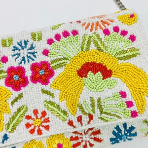 Pu&ograve; includere: Una pochette bianca con perline e un motivo floreale. I fiori sono gialli, rossi, rosa, arancioni e blu.