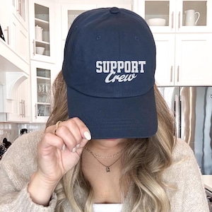 May include: A navy blue baseball cap with white embroidered text that reads "SUPPORT Crew".