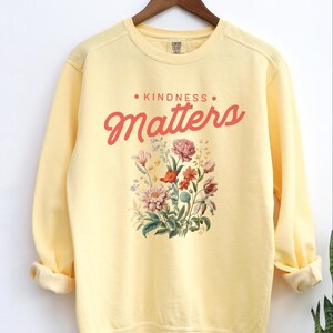 May include: Yellow sweatshirt with a floral design and the text "KINDNESS MATTERS" in red.