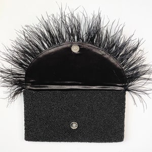 May include: A black beaded clutch with a black feather trim. The clutch has a half-circle flap with a snap closure.