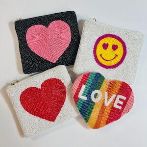 May include: Four beaded pouches with different designs. One pouch is black with a pink heart, one is white with a red heart, one is white with a yellow smiley face with pink eyes, and one is rainbow with the word "LOVE" in white.