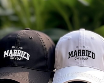 Może przedstawiać: Dwie czapki bejsbolowe, jedna czarna, a druga biała, z napisem "Officially Married Est 2025" w białym kolorze na czarnej czapce i czarnym kolorze na białej czapce.